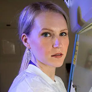 Headshot of Meghan Hermance (PhD) in front of a biosafety cabinet (BSC)