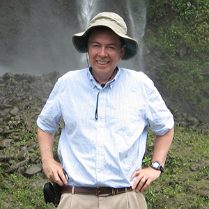 Picture of Abelardo Moncayo (PhD) standing outdoors in front of a waterfall and rocky landscape.