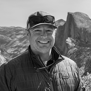 Black and white picture of Brian Byrd, PhD, standing in front of a mountain landscape.